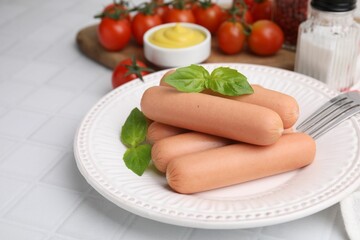Delicious boiled sausages and basil served on white tiled table, closeup