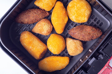 cooking in the air fryer delicious Brazilian snacks made inside the airfryer basket view from above on white background with selective focus (Coxinhas)