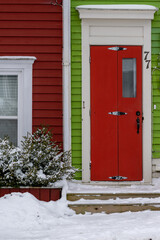 The exterior of a vibrant green wooden clapboard siding house with a colorful red bifold door....