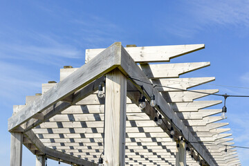 A grey colored worn and weathered wood pergola roof with a blue sky in the background. The outdoor...