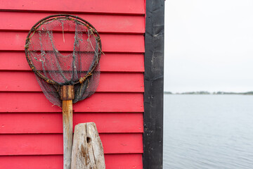 A vintage fishing dip net hanging on a vibrant red wooden horizontal clapboard wall. The scoop is...