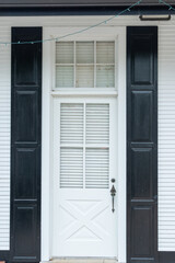 A navy blue wooden house wall with a half glass four-pane window in the panel exterior door. There's a metal doorhandle, transom window with white curtains. The doorway entrance is to a country house. - obrazy, fototapety, plakaty