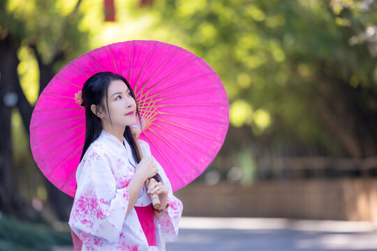 Asian woman wearing japanese traditional kimono. Beautiful Woman smiling, holding a umbrella walking outside. Woman in Kimono dress enjoying and walking on street outdoors in slow motion.