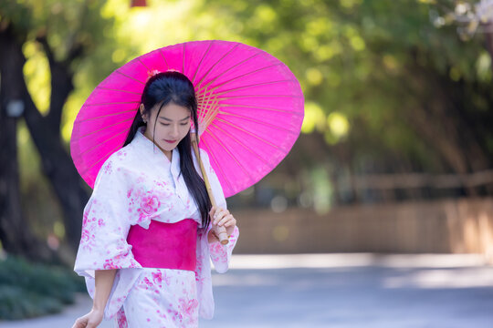 Asian woman wearing japanese traditional kimono. Beautiful Woman smiling, holding a umbrella walking outside. Woman in Kimono dress enjoying and walking on street outdoors in slow motion.