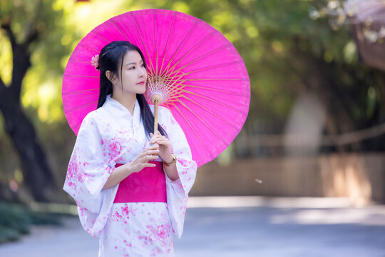 Asian woman wearing japanese traditional kimono. Beautiful Woman smiling, holding a umbrella walking outside. Woman in Kimono dress enjoying and walking on street outdoors in slow motion.