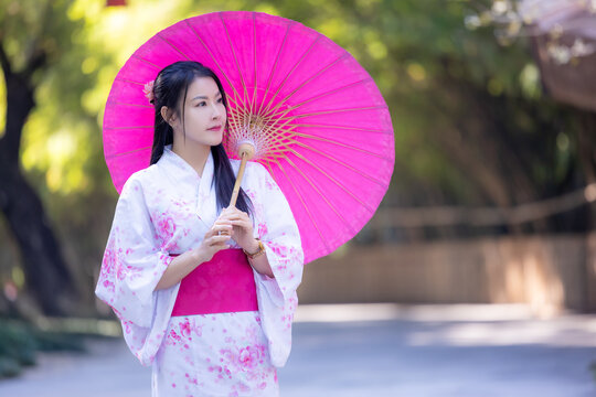 Asian woman wearing japanese traditional kimono. Beautiful Woman smiling, holding a umbrella walking outside. Woman in Kimono dress enjoying and walking on street outdoors in slow motion.
