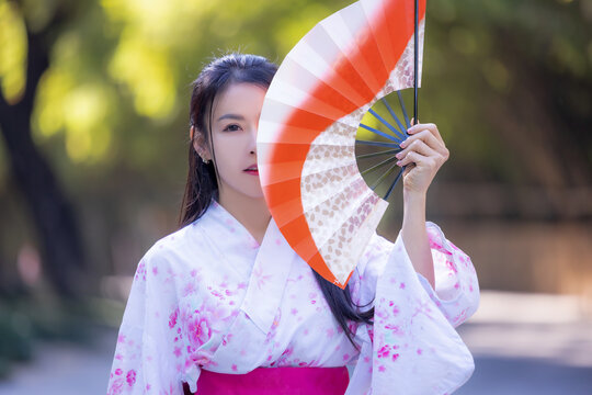Asian woman wearing japanese traditional kimono standing on street.Beautiful Woman smiling ,holding hand fan to cover face. Woman in Kimono dress enjoying and walking on street outdoors in slow motion