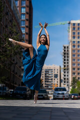 Beautiful Asian ballerina in blue dress posing in splits outdoors. Urban landscape. Vertical photo. 