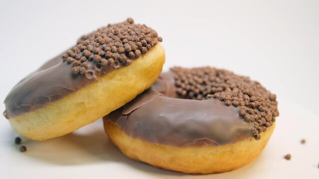 Two donuts coated with milk chocolate icing and flakes rotate in a circle on a white background.