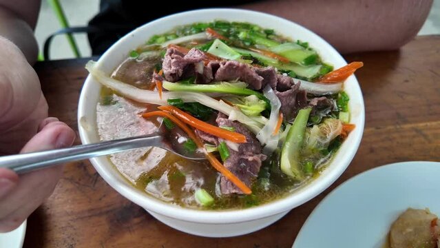 Traditional Vietnamese pho soup with sliced beef, rice noodles, and vegetables, served in a bowl with chopsticks, representing Vietnamese cuisine