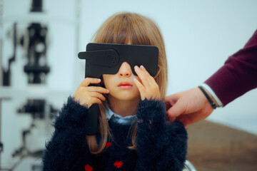 Little Patient Girl Holding a Lorgnette Pinhole occluder for Consultation