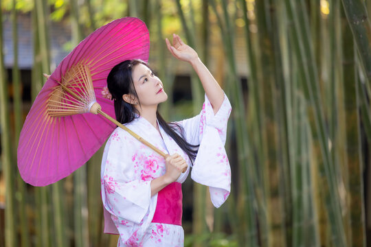 Asian woman wear Japanese kimono holding umbrella walking in the bamboo forest.Woman in Kimono dress enjoying,walking on street outdoors in slow motion.Beautiful Woman standing on street.