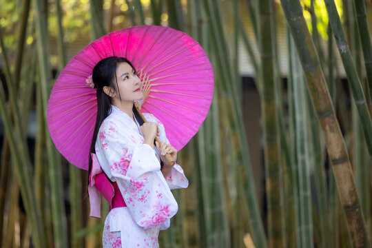 Asian woman wear Japanese kimono holding umbrella walking in the bamboo forest.Woman in Kimono dress enjoying,walking on street outdoors in slow motion.Beautiful Woman standing on street.