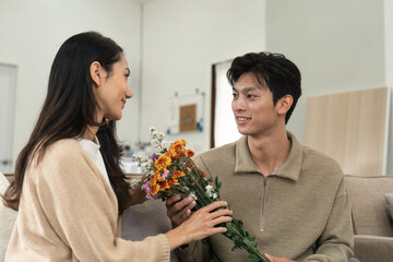 Asian handsome man show the love and give flowers to his girlfriend in living room on valentine day. Lifestyle Concept