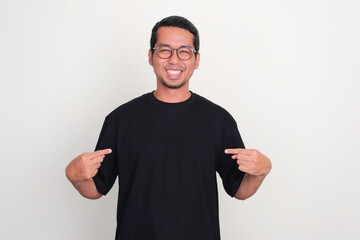 A man smiling at the camera while pointing to plain black t-shirt that he wearing