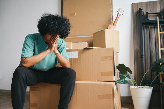 Tired unhappy Asian man moving out from apartment. Sad evicted man worried relocating house 