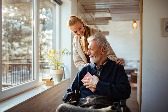 Young daughter pushing her father in a wheelchair at home