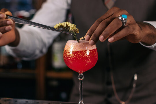 Close-up of an unrecognizable black bartender pouring a cocktail and decorating it with garnish