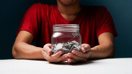 man with coins in a clear, transparent glass jar in his hand. saving money concept