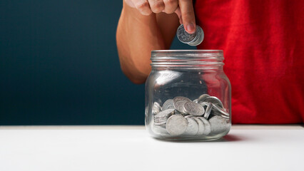 man puts coins in a clear transparent glass jar