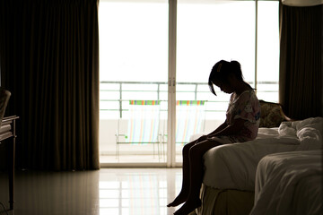 silhouette of a sad little girl sitting in bed at home, family problems. fear and fobies of child. Psychological portrait of scared young girl.