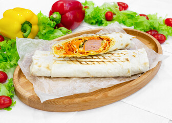 Shawarma, doner with sausage, carrots, cucumber and vegetables on a wooden board