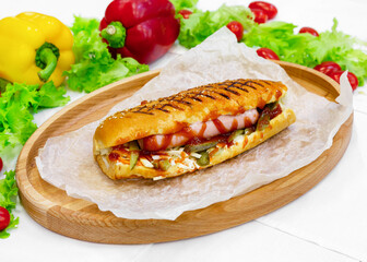 Hot dog, bun with sausage, carrots, cucumber and vegetables on a wooden board
