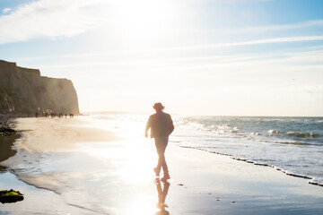 The image presents a lone individual embarking on a leisurely walk along the shoreline, with the dawn sun casting a diffuse light across the scene. This time, the person appears closer and more