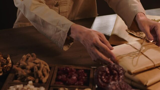 Front view of the physician wrapping each medicine package with string. The table displays many precious medicinal herbs in traditional medicine. Slow motion with commercial scene.
