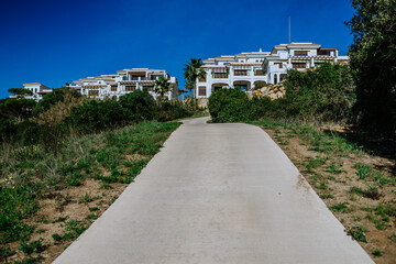 Sotogrande, Spain - January, 23, 2024 - A concrete pathway leading up to a complex of white Mediterranean-style buildings with blue sky above.