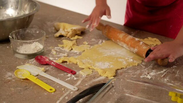 manos de niña vestida de rojo amasando harina para preparar y hornear galletas o pan casero con utensilios de cocina rodillo