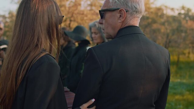 Back footage of young lady coming up to senior father and giving condolences at outdoor funeral ceremony