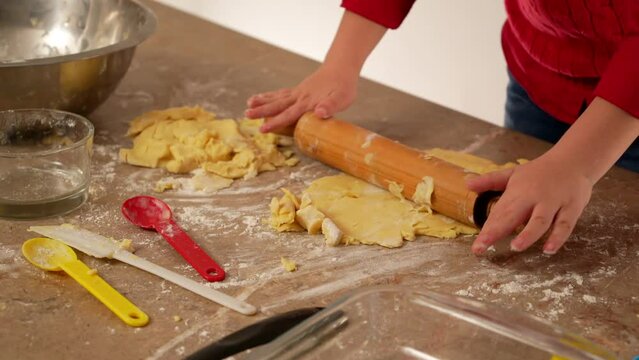 manos de ni&ntilde;o vestido de rojo amasando harina y preparado para hornear galletas o pan casero con utensilios de cocina rodillo y con instrumentos y recipientes