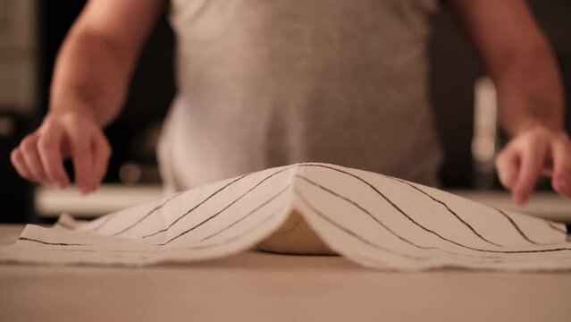 Man covering bread dough with stripped kitchen cloth before letting it rise.