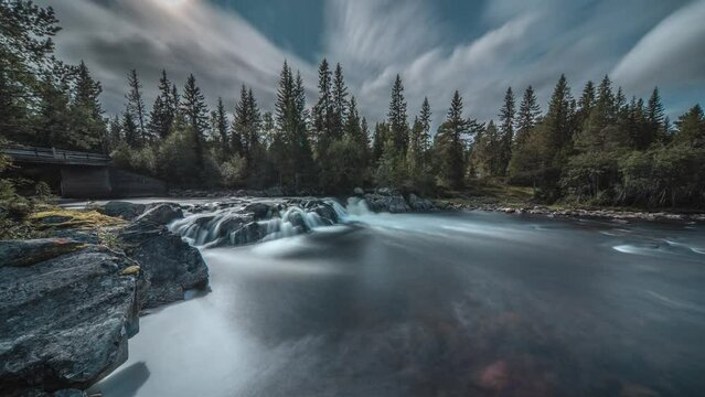 A long exposure video of the shallow mountain river with a small waterfall. Changing clouds fly above.