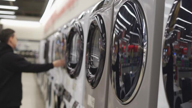 Man in the store choosing the washing machine. Open the door of the washing machine