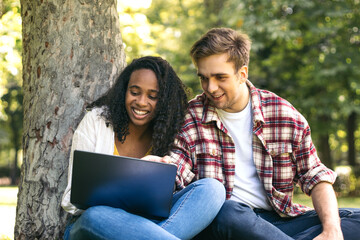 Multiracial couple studying in the park with laptop