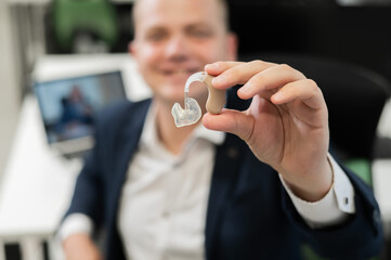 Deaf man working holds hearing aid while sitting in office.