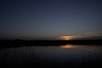 Obraz premium This image offers a minimalist view of dusk's final moments, where the last streaks of sunlight cast a subdued glow on the horizon. The sky transitions from the warm tones of the fading sun to the