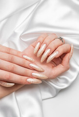 Female Hands on a white silk background with beautiful pearl manicure.Hands on a brown background and beautiful pearl manicure