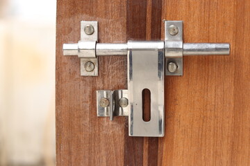 A close-up view of a weathered silver metal door latch on an aged wooden door, shining, bokeh
