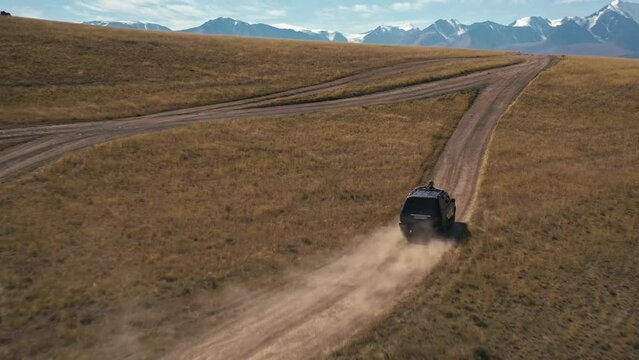 Automobile travel adventure driving on dirt road at field rocky terrain snowy mountain landscape FPV drone shot. Female enjoy freedom win victory on roof auto vehicle transportation at cliff scenery