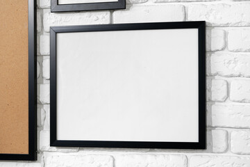 Black picture frame hanging on white brick wall copy space