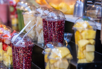 Fresh pomegranate seeds and pineapple pieces in plastic transparent cups for sale at the farmers market - 723576849