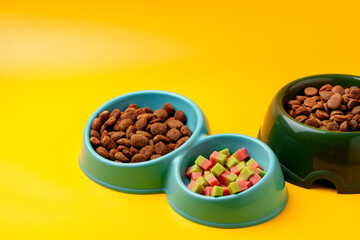 Bowl with dry pet food on yellow background studio shot