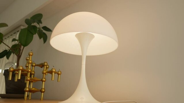Modern white lamp with a golden structure on a wooden shelf.