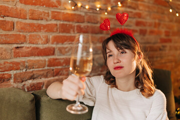Young beautiful woman celebrating valentine day drinking a glass of champagne sparkle wine wearing heart shape funny decoration and cute white dress