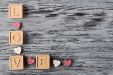 Word ‘LOVE’ spelled out with wooden blocks and adorned with small red hearts on textured wooden...