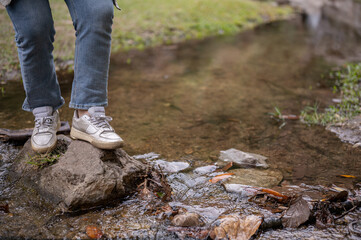 A close-up image of an adventure woman crossing a small nature canal while hiking on the mountain.