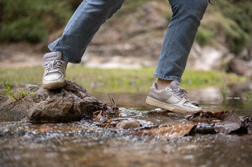 A close-up image of an adventure woman crossing a small nature canal while hiking on the mountain.